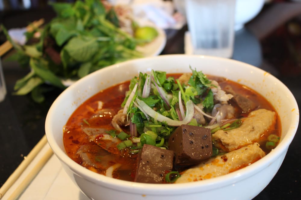 Spicy noodle soup with beef and a plate of herbs