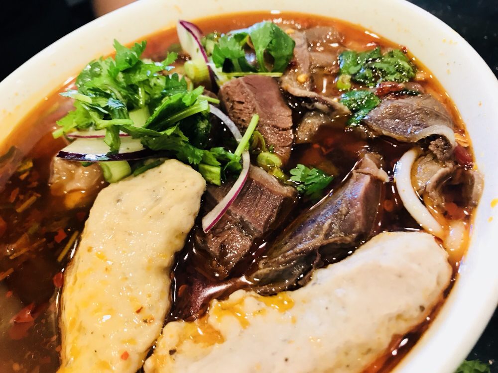 Spicy beef noodle soup with sliced beef, pork cake and fresh herbs